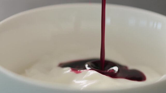 Slow motion pour blueberry juice over natural yogurt in white bowl closeup