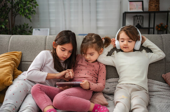 Young girls relaxing on sofa using digital tablet and headphones