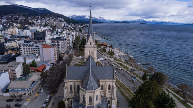 Aerial view of the Catedral de San Carlos de Bariloche with stone architecture, urban cityscape, and Nahuel Huapi Lake in San Carlos de Bariloche, Rio Negro Province, Argentina.