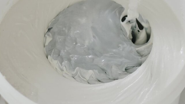 Slow motion closeup mixing black ink into decorative concrete plaster to make gray