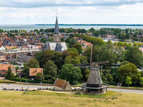 Aerial view of De Herder windmill and Bonifacius church with the IJsselmeer in the background, surrounded by trees and rooftops in Medemblik, Noord-Holland, Netherlands.