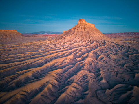 Aerial view of Factory Butte rising above the rugged, eroded badlands of the desert landscape under a clear blue sky in Wayne County, Utah, United States.