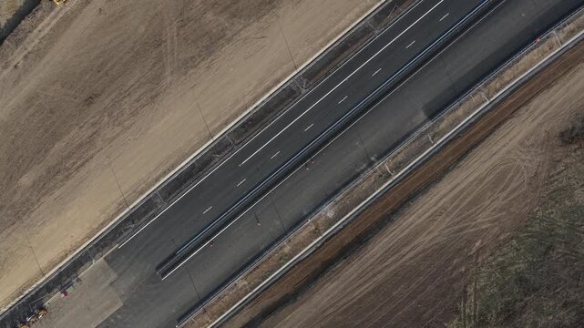 Top down aerial view of Autostrada Moldovei A7 Nod Bacau construction site showing fresh asphalt lanes, heavy road building machinery, and infrastructure progress. 4K video.