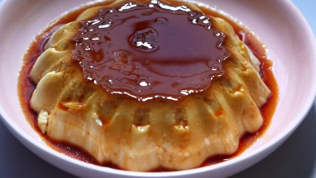 Close up motion of traditional caramel flan custard dessert served on pink plate with golden syrup topping