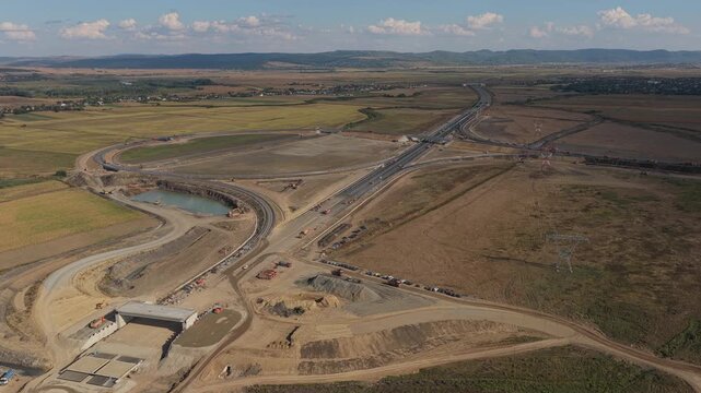Aerial panoramic view of highway construction at Autostrada Moldovei A7 junction near Bacau under bright daylight, highlighting modern infrastructure development. 4K video.