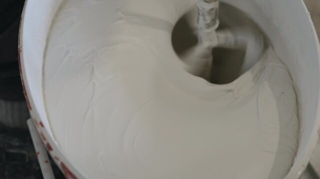 Slow motion closeup mixing black ink into decorative concrete plaster to make gray