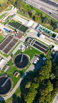 Aerial view of the wastewater treatment plant with circular sedimentation tanks, rectangular filtration basins, and surrounding green areas near a highway in San Giuliano Milanese, Lombardia, Italy.