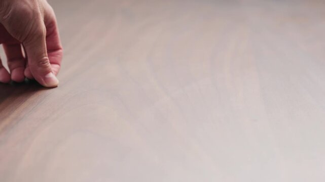 Slow motion of man hand checking toned walnut table surface with oil finish