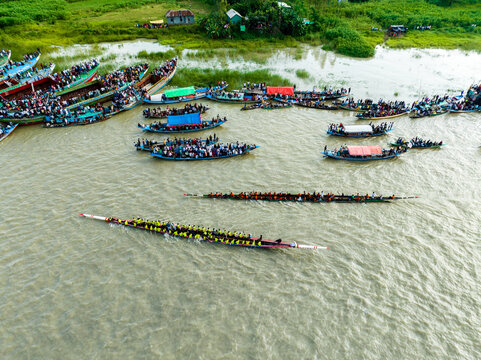 Aerial view of a traditional boat race with long narrow vessels filled with rowers and spectators on boats along the riverbank in Manikganj, Dhaka Division, Bangladesh.