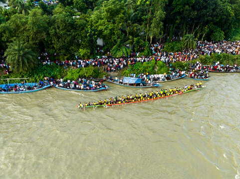 Aerial view of a traditional boat race on a river with numerous spectators gathered along the lush riverbank and people watching from wooden boats in Manikganj, Dhaka Division, Bangladesh.