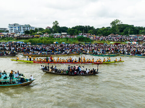 Aerial view of a traditional boat race on the river with many rowers in long wooden boats and large crowds gathered along the riverbank in Manikganj, Dhaka Division, Bangladesh.