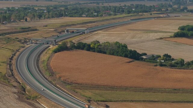 Aerial view of the new A7 Autostrada Moldovei highway under construction near Bacau, crossing rural agricultural fields under clear daytime sunlight. 4K video.