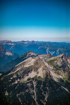 Aerial view of the Zugspitze mountain range near Eibsee, featuring rugged peaks, rocky slopes, and deep green forested valleys in Grainau, Bayern, Germany.