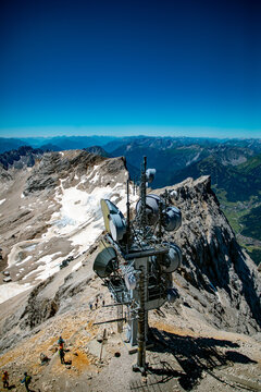 Aerial view of the communication tower on the summit of Zugspitze with rocky terrain, snow patches, and hikers in the Bavarian Alps, Grainau, Bayern, Germany.