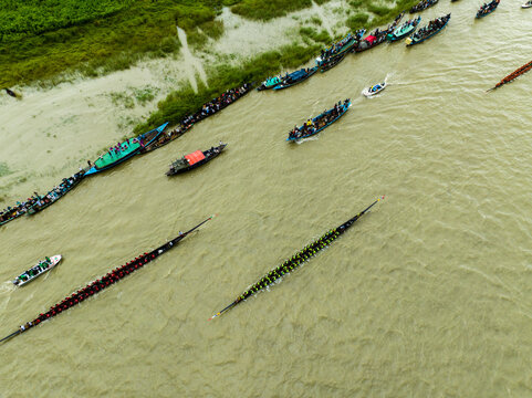 Aerial view of a traditional long boat race on the river with many spectators in boats moored along the bank in Manikganj, Dhaka Division, Bangladesh.
