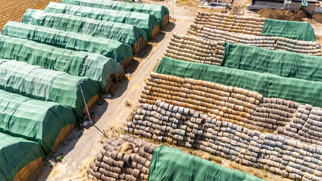Aerial view of large stacks of hay bales protected by green tarps arranged in rows on a farm in Sabac, Vojvodina, Serbia.