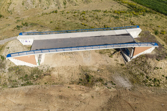 Aerial view of a bridge construction site for a bypass road, featuring concrete structures, blue railings, and surrounding rural landscape in Celle, Germany.