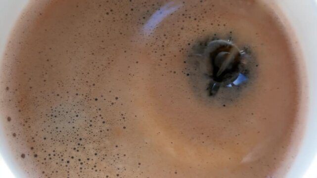 Drops of black cumin oil fall into fresh black morning coffee, slow motion.