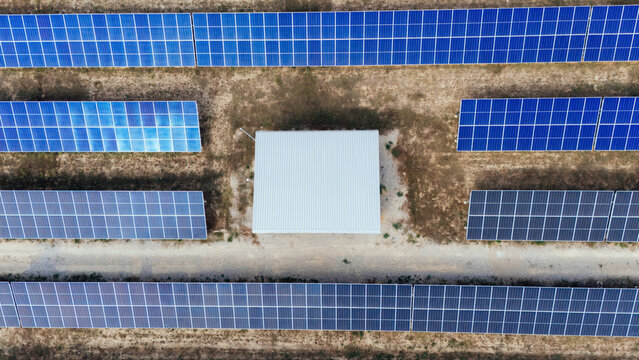 Aerial view of a solar farm with rows of blue photovoltaic panels and a central white utility building in a rural landscape Sabac, Vojvodina, Serbia.