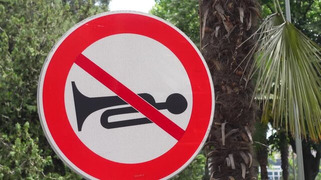 No honking traffic sign in motion with lush green trees and palm fronds in background