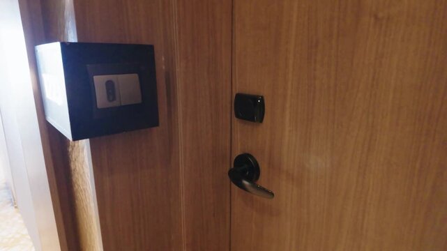 Wooden hotel room entrance door with electronic keycard lock and digital sensor wall switch.