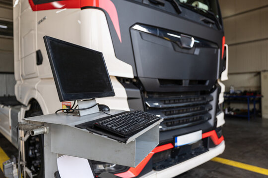 Truck service.  Computer diagnostic workstation in modern truck service garage station with heavy semi truck undergoing wheel alignment and technical maintenance checkup.