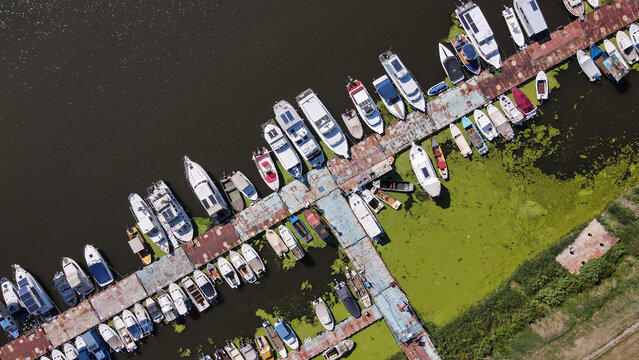 Aerial view of numerous boats docked at the Ada Ciganlija marina, with calm water covered in green algae and weathered wooden piers in Belgrade, City of Belgrade, Serbia.
