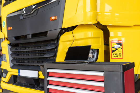 Truck service.  Modern yellow heavy truck undergoing computerized diagnostic inspection in an automotive workshop with laptop resting on professional mechanical tool cart.