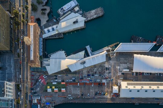 Top-down aerial view of Queens Wharf in Auckland, New Zealand, showcasing waterfront architecture, docks and ferry terminals at sunrise.
