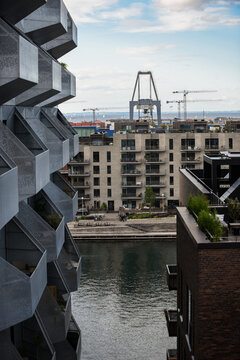 Aerial view of a modern residential building with geometric balconies overlooking a canal with a harbor crane in the background in Copenhagen, Denmark.