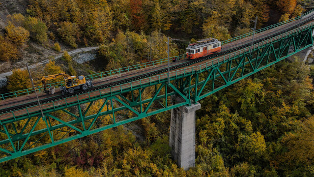 Aerial view of a train and an excavator on the green Mala Rijeka Viaduct surrounded by autumn forest in Montenegro.