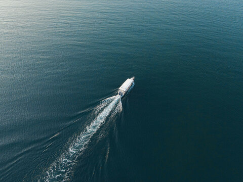 Aerial view of a small white boat cruising through the deep blue waters of Raja Ampat, leaving a white wake behind it in Southwest Papua, Indonesia.