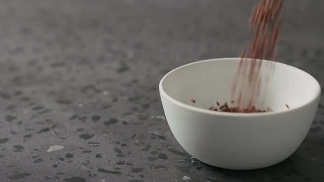 Slow motion flaxseed falling into white bowl on terrazzo countertop