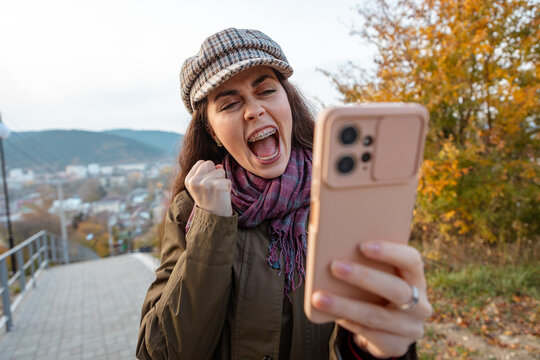 Caucasian female smiling with excitement after seeing a positive notification on mobile phone. Good fortune and celebration concept.