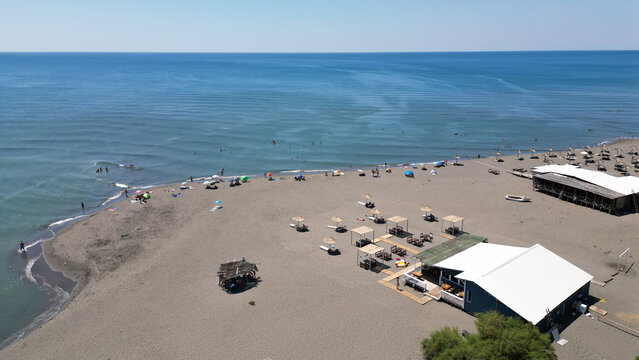 Aerial view of Ada Bojana beach with rows of umbrellas, a restaurant building, and people relaxing on the sand along the Adriatic Sea in Ulcinj Municipality, Montenegro.