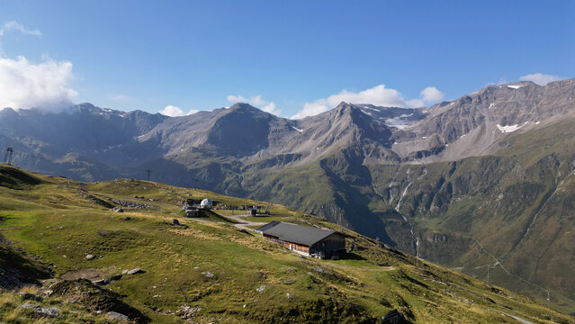Aerial view of Sportgastein in the Austrian Alps, featuring a mountain hut, grassy slopes, and rugged peaks under a clear blue sky in Bad Gastein, Salzburg, Austria.