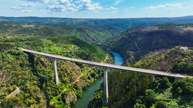 Aerial view of a concrete viaduct spanning a lush green river valley with a winding river below in Portugal.