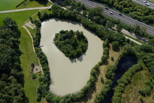 Aerial view of a pond with a central island surrounded by lush greenery and trees near the Dwingelerveld National Park and the highway A28 in Spier, Drenthe, Netherlands.