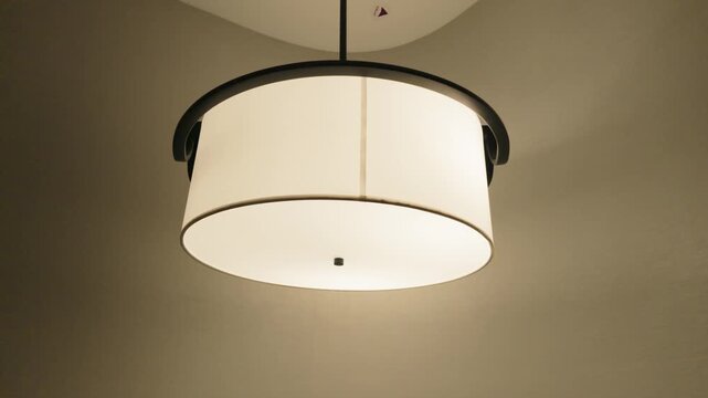 Modern round drum pendant lamp glowing softly on ceiling in contemporary interior room.