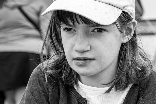 Black and white close-up portrait of a young girl wearing a baseball cap with a thoughtful, serious expression.