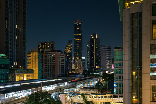Aerial view of the illuminated King Power Mahanakhon skyscraper and Surasak BTS station at night, surrounded by modern urban buildings and city lights in Bangkok, Bangkok, Thailand.