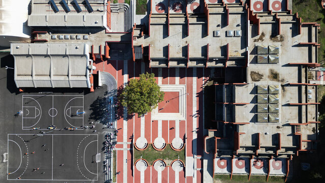 Aerial view of the brutalist architecture of Block 63 in Belgrade, featuring a central courtyard, geometric red and white paving, a basketball court, and a tree, Belgrade, City of Belgrade, Serbia.