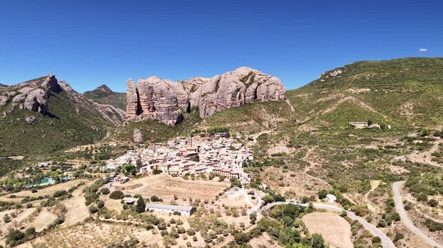 Cinematic aerial drone footage of the vast, sweeping landscape surrounding Ag&uuml;ero, with the iconic, towering conglomerate rock formations of the Mallos de Ag&uuml;ero rising majestically in the background 
