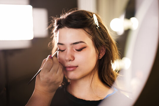 Close-up shot of cosmetics brush blending brown eye shadow onto eyelid during beauty makeover session in professional studio.
