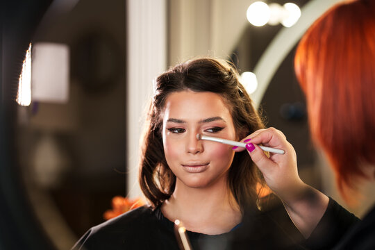 Close-up shot of a skilled beauty specialist using a brush for facial styling and glamorous makeover in a brightly lit professional salon environment.