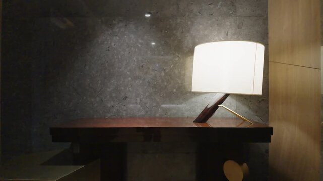 Modern interior with elegant glowing table lamp on dark wooden desk against stone wall.