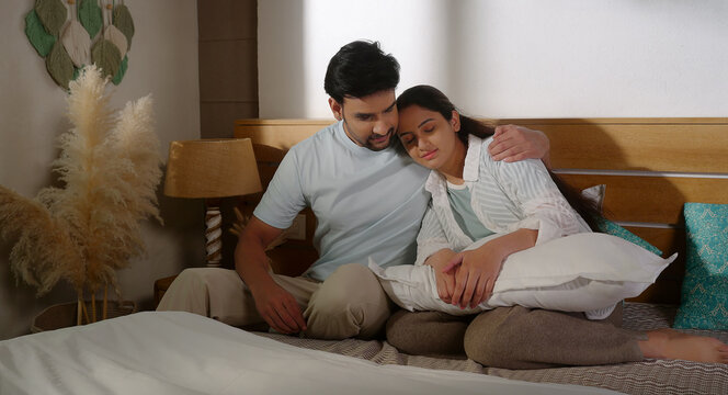Indian young adult gen z male female pair couple sitting cozy bed hold hand do patch up share love care happy man woman talk speak take rest on shoulder spend time enjoy indoor room place