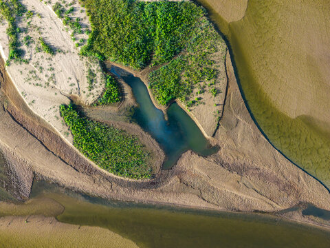 Aerial view of low water levels in a river bed with exposed sandbanks and patches of green vegetation in Poland.