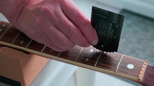 Hand adjusts guitar fretboard with precision tool to measure fret hight. Close-up shows meticulous instrument maintenance. Professional care emphasizes craftsmanship and accuracy. Ideal for music, rep