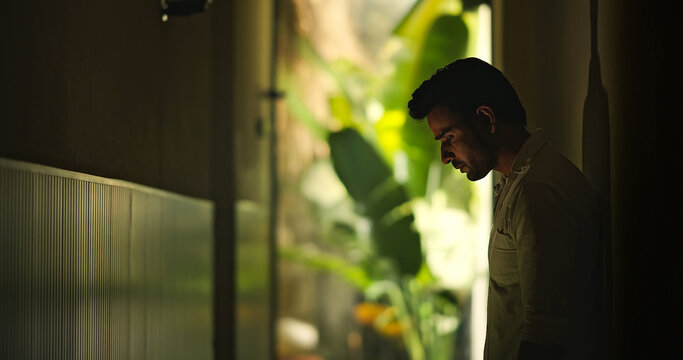 Indian young adult gen z sad stress man guy look upset feel bad hurt head ache in dark living room. Alone tired male boy think deep suffer low health issue lost job fail guilt indoor house home place
